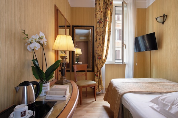 A hotel room with a bed, a desk with a lamp, a chair, a television, and a window with curtains. - Hotel Cecil (Rome)