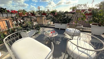 Una terraza en la azotea con mobiliario exterior, plantas en macetas y un cielo despejado.