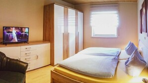 A bedroom with a bed, a TV on a dresser, a wardrobe, and a window.