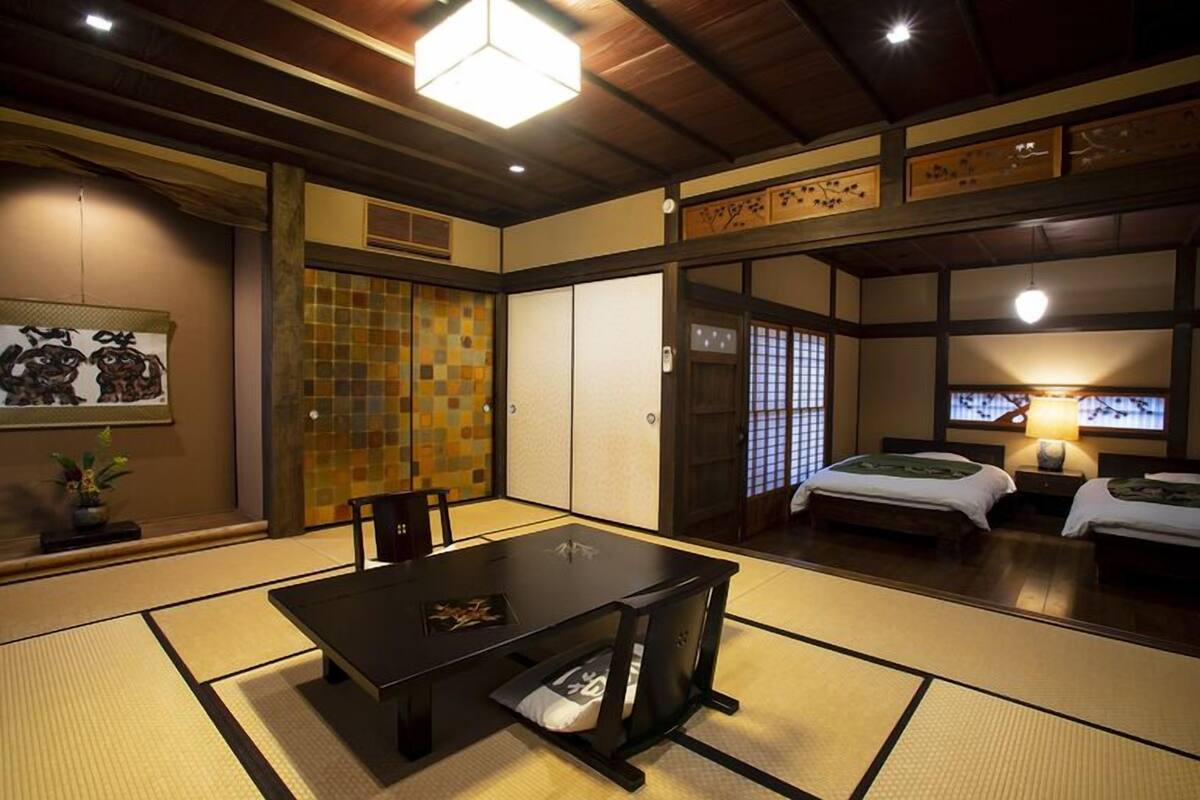 Ein traditioneller japanischer Raum mit Tatami-Boden, niedrigem Tisch, Schiebetüren und einem Bett mit Futon.