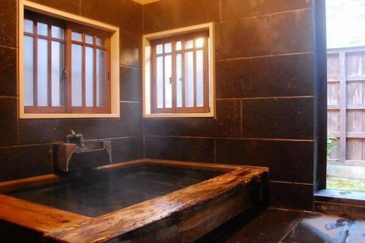 Ein Zimmer mit einer Holzwanne, dunklen Fliesenwänden und Fenstern mit Holzrahmen.
