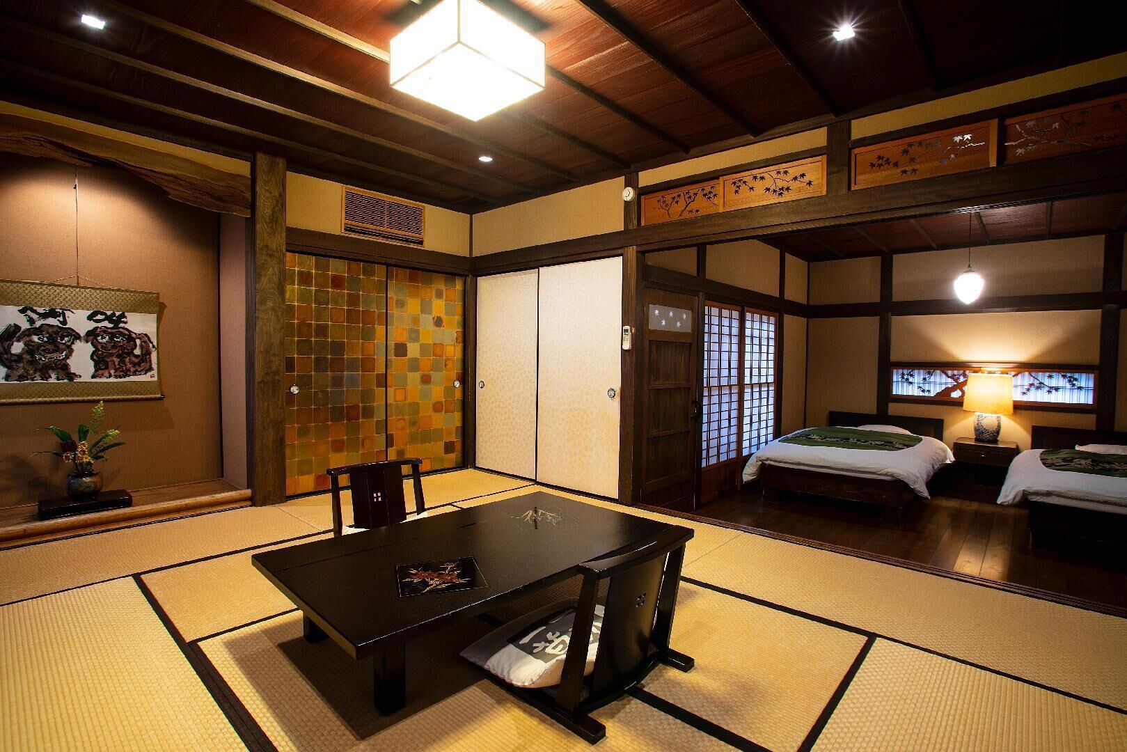 Una habitación tradicional japonesa con suelo de tatami, una mesa baja, dos camas y puertas correderas.