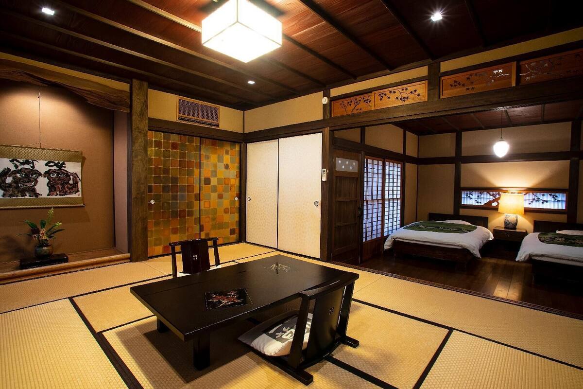 Ein traditioneller japanischer Raum mit Tatami-Bodenbelag, einem niedrigen Tisch, zwei Betten und einer Schiebetür.