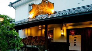 A traditional Japanese building with a wooden sign, a covered porch, and a stack of logs. - Hirayama Onsen Yama Futokoro no Yado Ichiboku Isso (Yamaga)