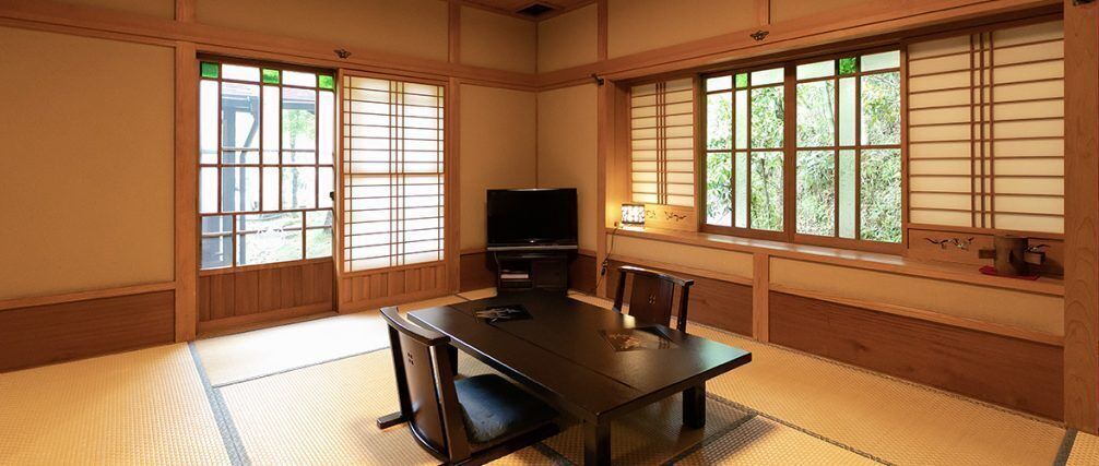 Una habitación japonesa tradicional con suelo de tatami, una mesa baja, un televisor y puertas correderas.