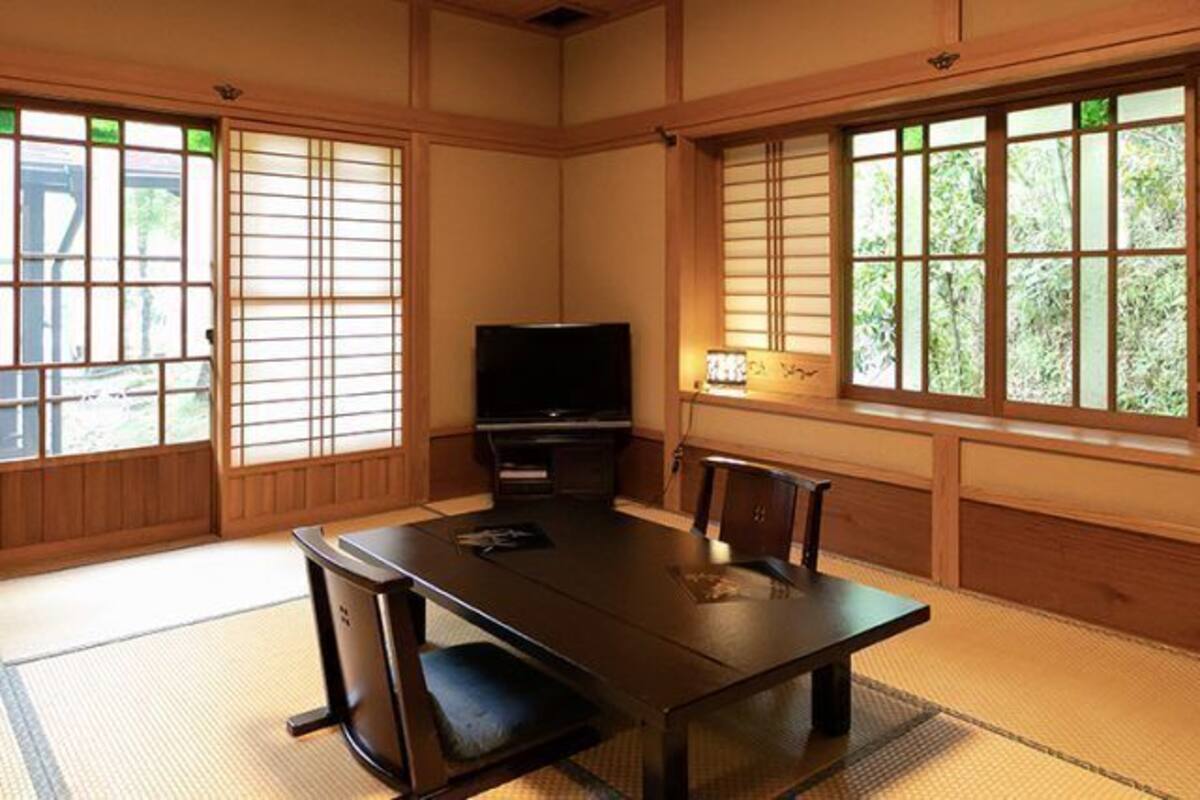 Ein traditioneller japanischer Raum mit Tatami-Boden, einem niedrigen Tisch, einem Fernseher und Schiebetüren.