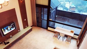 Una sala de estar moderna con un televisor de pantalla plana, una mesa de centro de madera, un sofá y un ventanal que ofrece vistas al exterior.