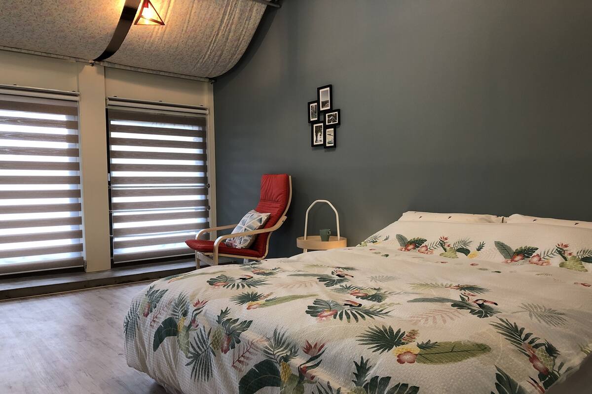 Un dormitorio con una cama, una silla, una repisa en la pared y una ventana con persianas.
