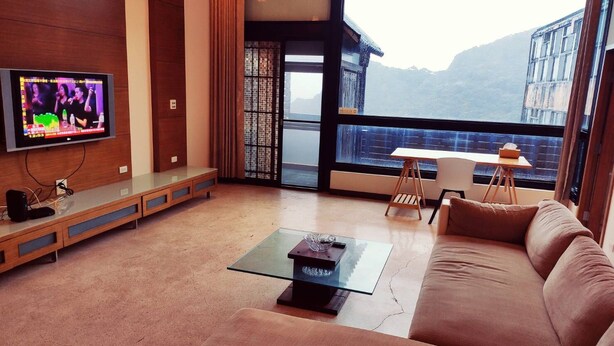 Una sala de estar moderna con televisor, una mesa de centro de cristal, sofá y vistas a las montañas a través de amplios ventanales.