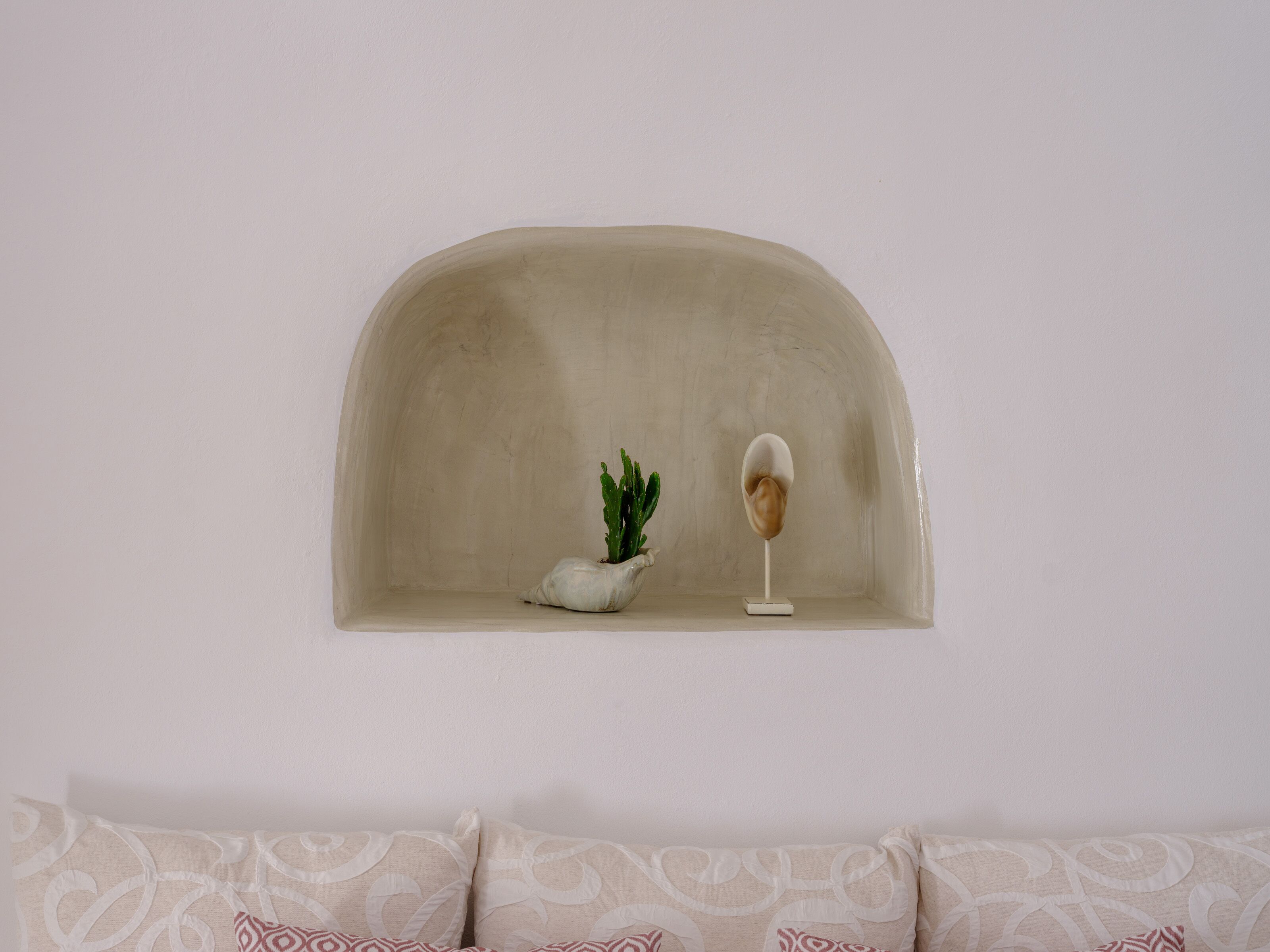 A white wall with a recessed shelf containing a small cactus and a decorative object.