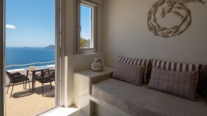 A balcony with a view of the sea, a sofa with patterned cushions, and a decorative wall piece. - Strogili Traditional Houses (Santorini)