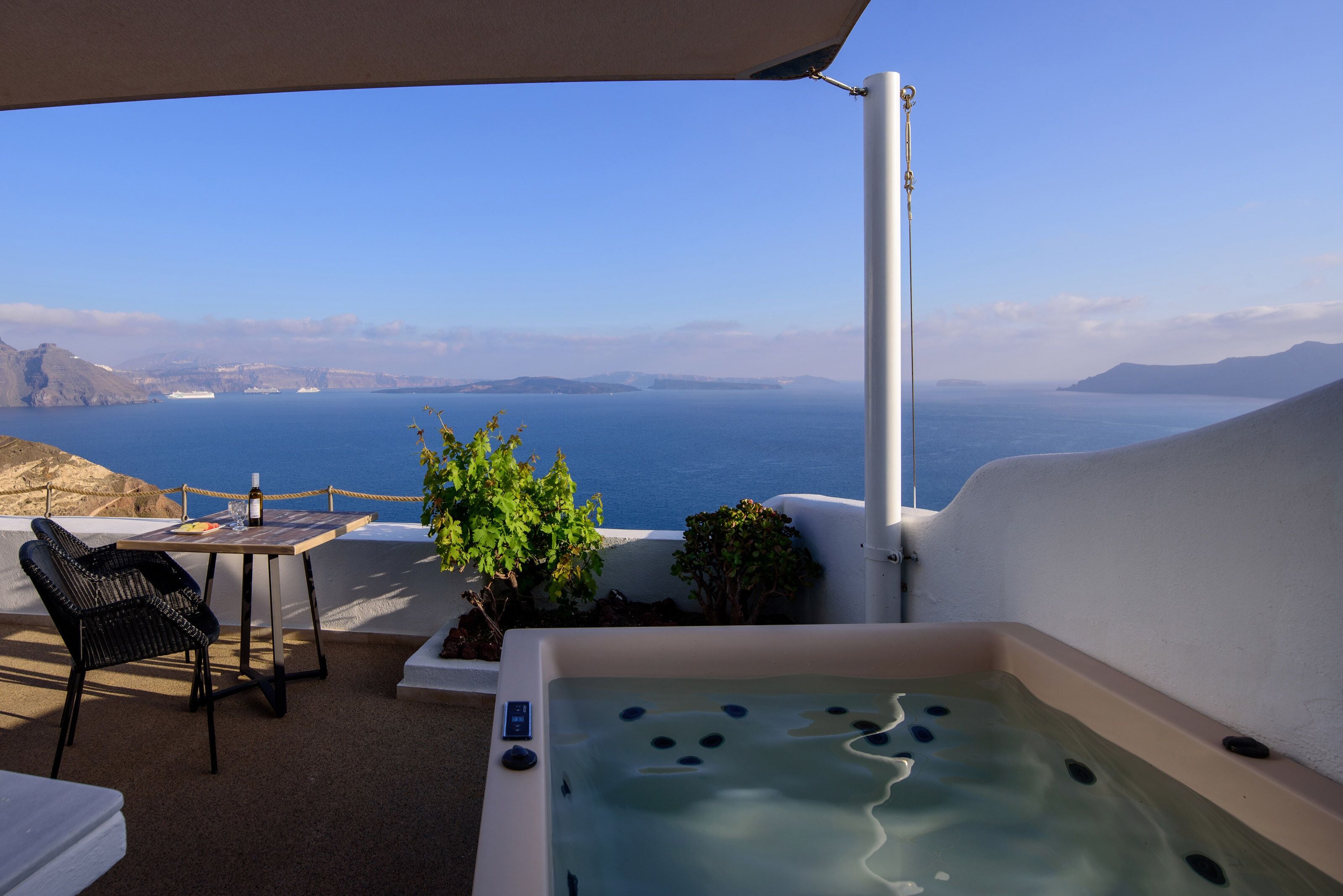 A hot tub with a view of the sea, a table with a chair, and a rope barrier.