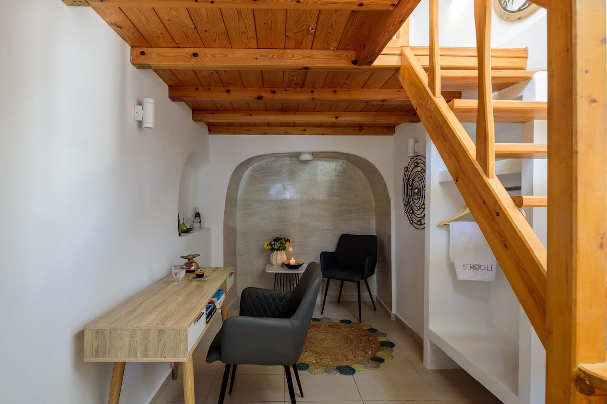 A narrow hallway with a wooden staircase on the right, a dining area with a table and chairs on the left, and a small table with a vase and candles in the center.