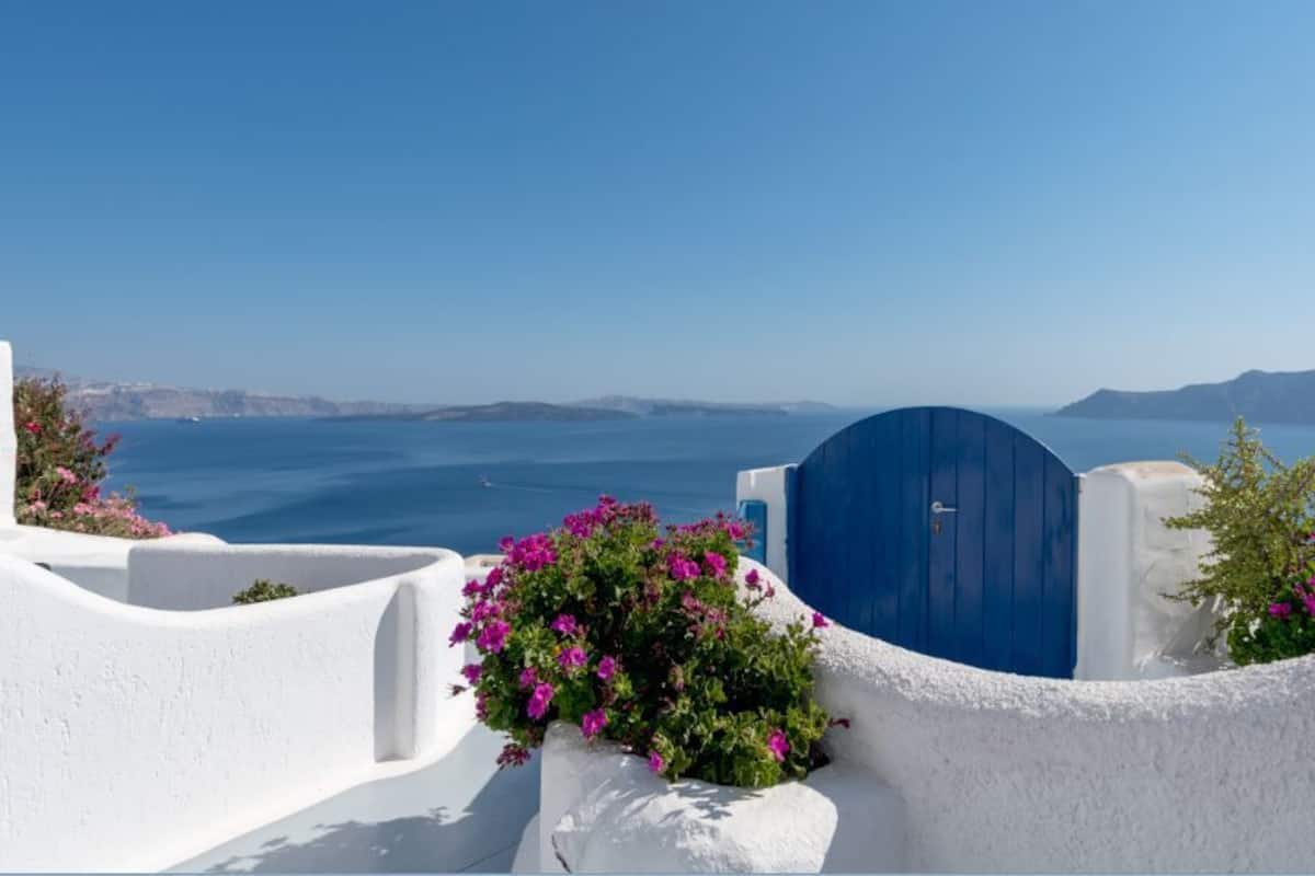 A white-walled building with a blue door and pink flowers.