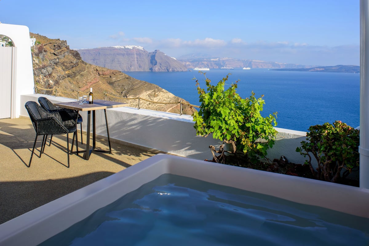 A balcony with a view of the sea and mountains, a hot tub, and outdoor seating.