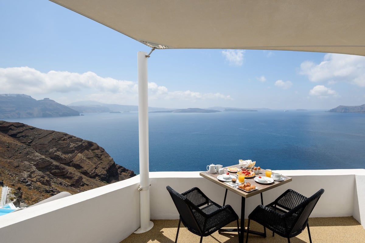 A balcony with a table set for breakfast overlooking a scenic view of the sea and distant islands.
