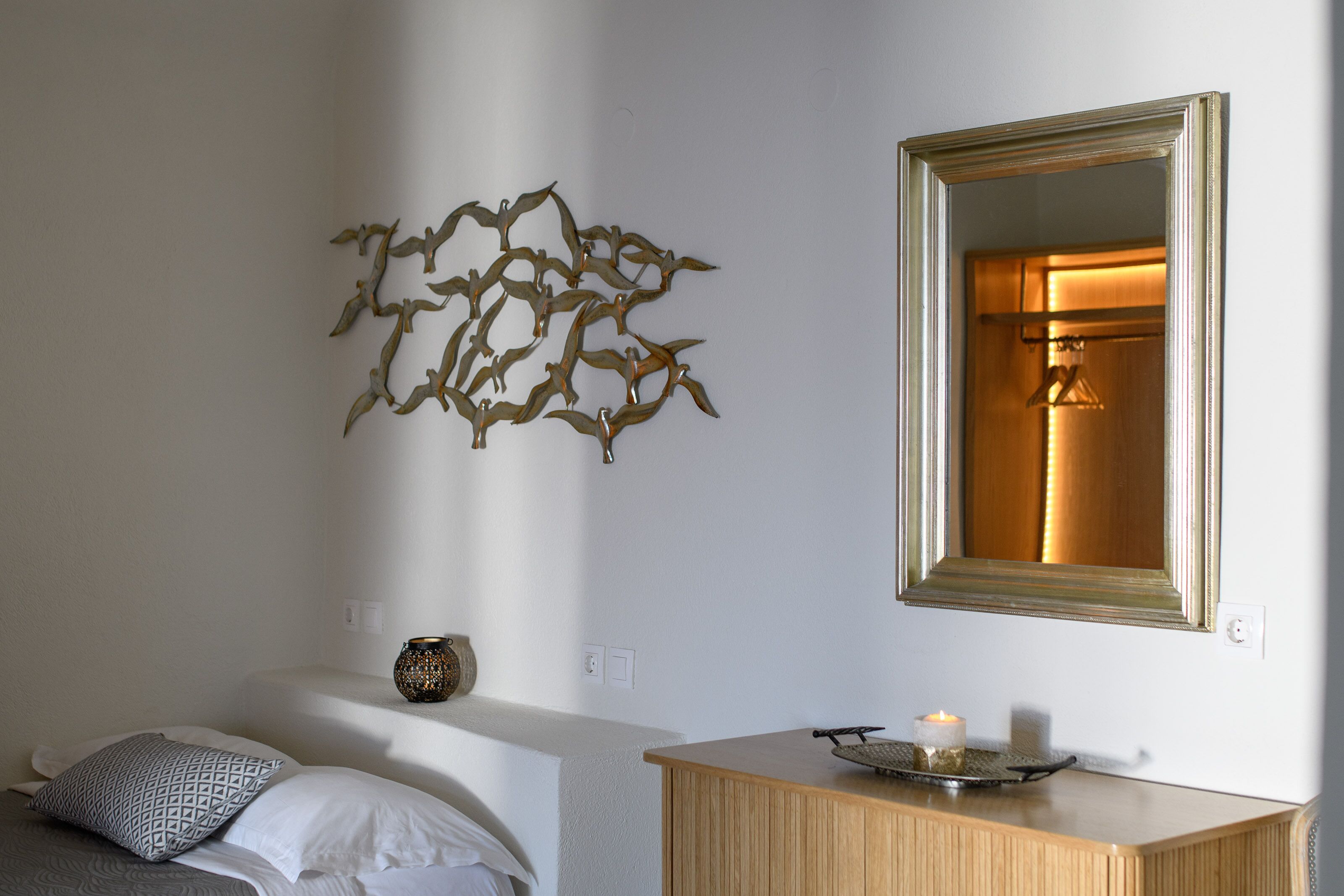 A room with a bed, a bedside table with a candle, a decorative wall piece, and a mirror.