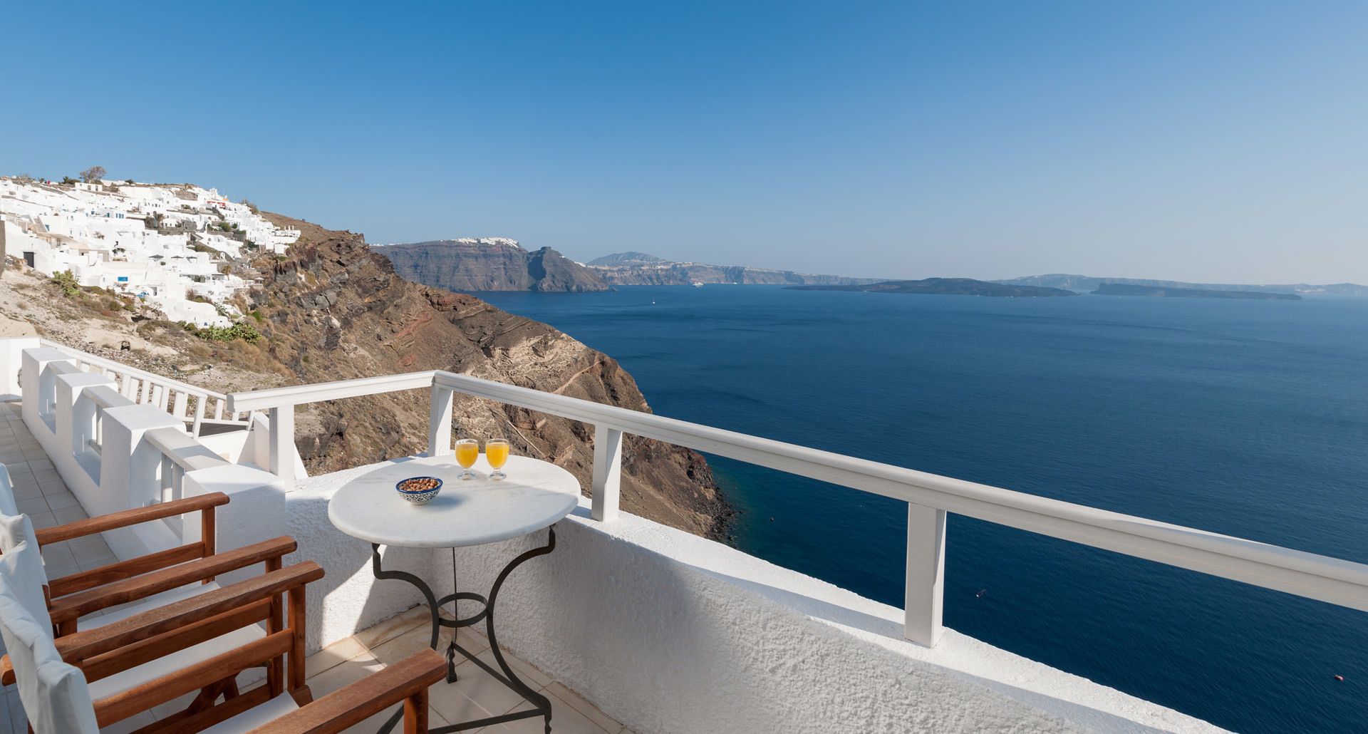 Ein Balkon mit Tisch, Stühlen und Blick auf das Meer und weiße Gebäude.