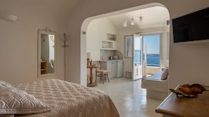 A bedroom with a large bed, a dining area, and a view of the sea. - Strogili Traditional Houses (Santorini)