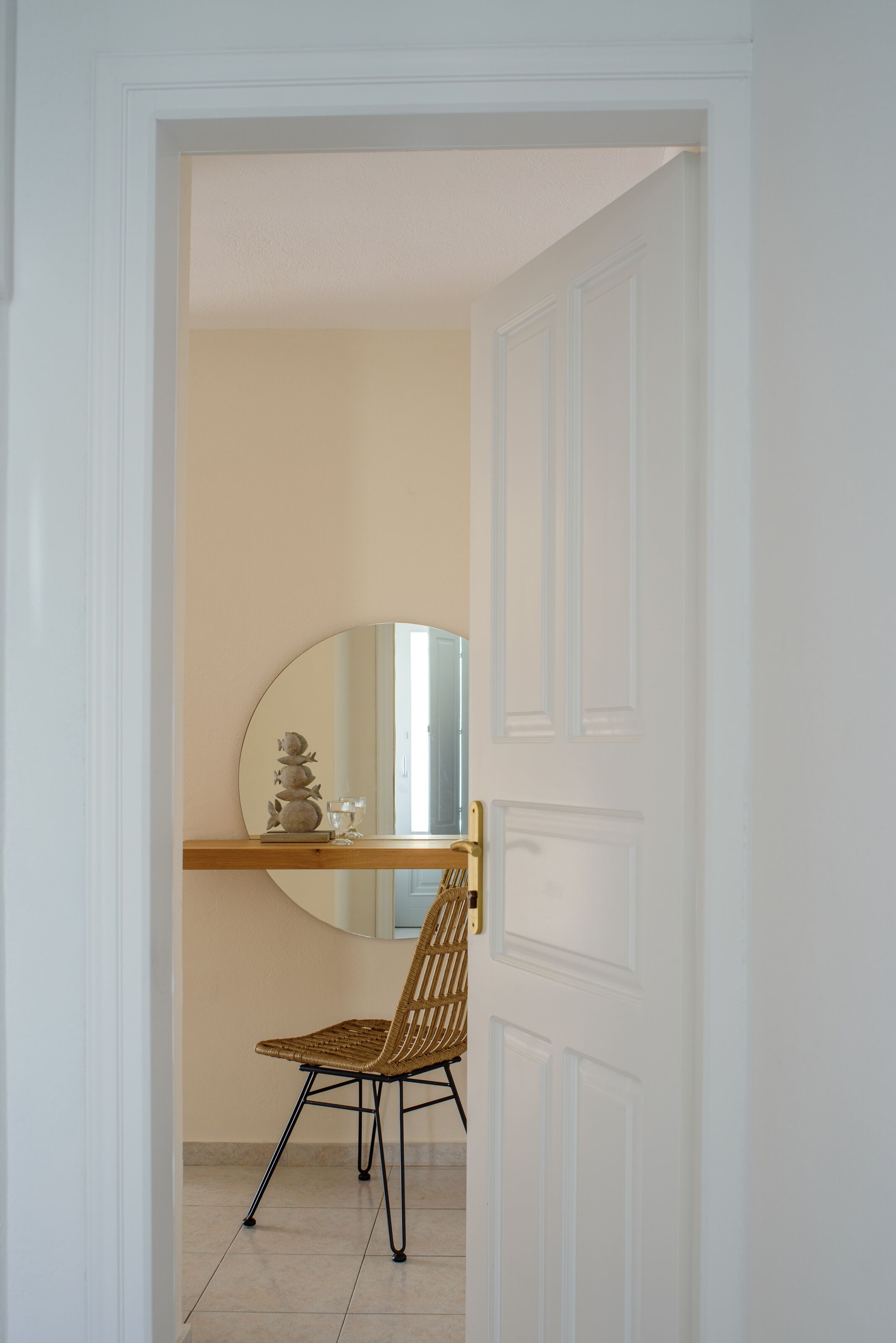 Una puerta que da a un cuarto con un espejo, un estante de madera y una silla de mimbre.