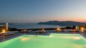 A pool area with lounge chairs and a view of the sea at dusk. - Strogili Traditional Houses (Santorini)
