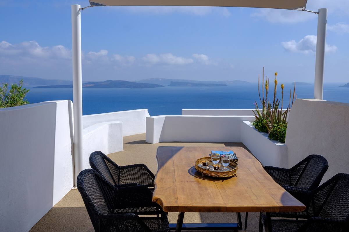 A terrace with a wooden table, two black wicker chairs, and a white umbrella.