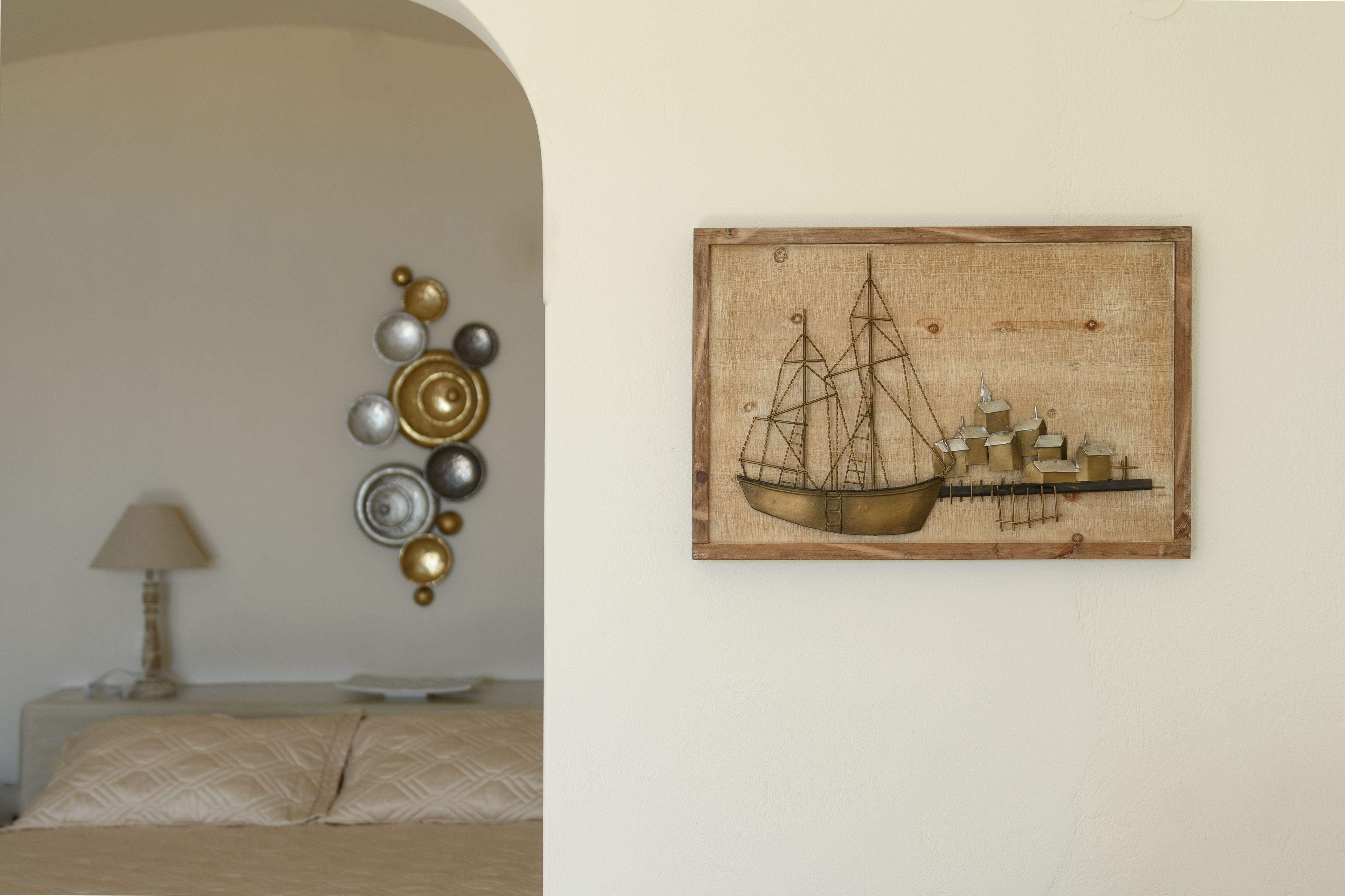 A bedroom with a bed, a wall-mounted decorative piece, and a framed artwork of a sailing ship.