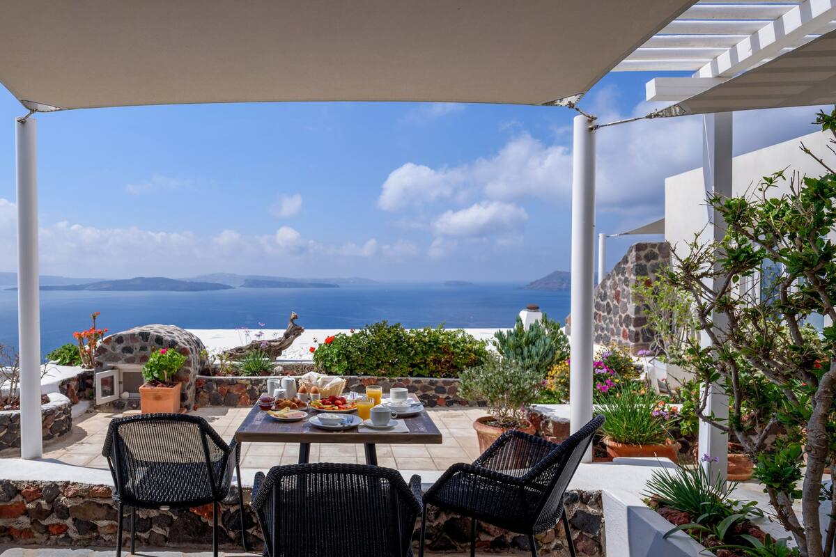 A terrace with a table set for breakfast, overlooking a scenic view of the sea and islands.