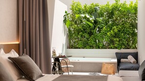 A modern hotel room with a bed, a sofa, a small table with a drink, and a large green plant wall. - Evanik Chic Hotel (Kalymnos)