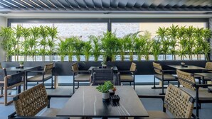 A rooftop restaurant with multiple tables and chairs, surrounded by potted plants and a stone wall. - Evanik Chic Hotel (Kalymnos)