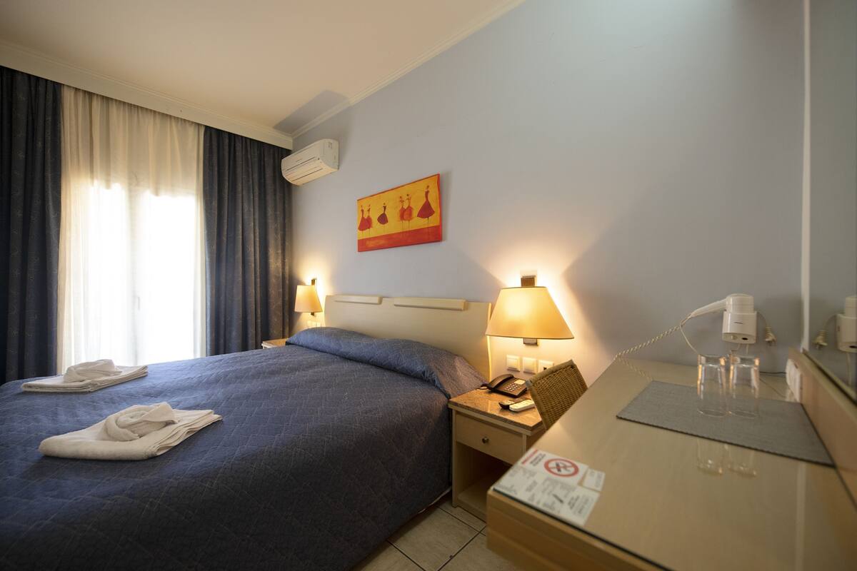 Ett hotellrum med en säng, sänglampor, en telefon, en spegel och en tavla på väggen.