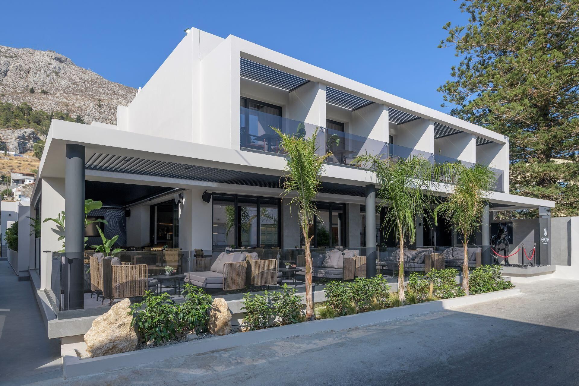 Un edificio moderno de dos pisos con techo plano, amplios ventanales y una zona de estar exterior cubierta con mobiliario.