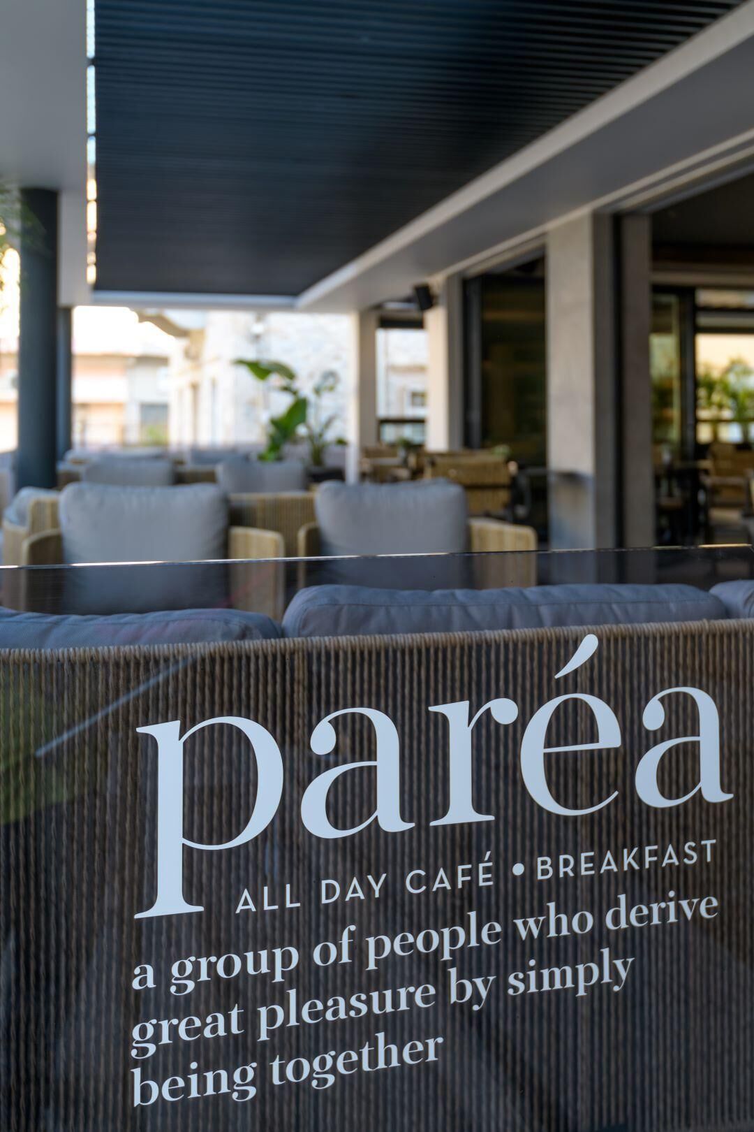Un área de estar al aire libre con un letrero que dice "parea all day café breakfast" y el lema "un grupo de personas que obtienen gran placer al estar simplemente juntas."