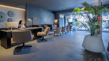 A modern hotel lobby with a reception desk, seating area, and large windows.