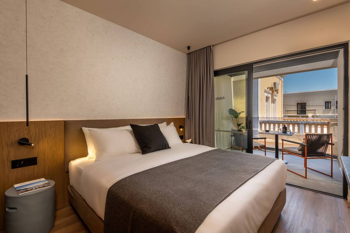 Ett modernt hotellrum med en stor säng, ett litet bord och en balkong med utsikt.