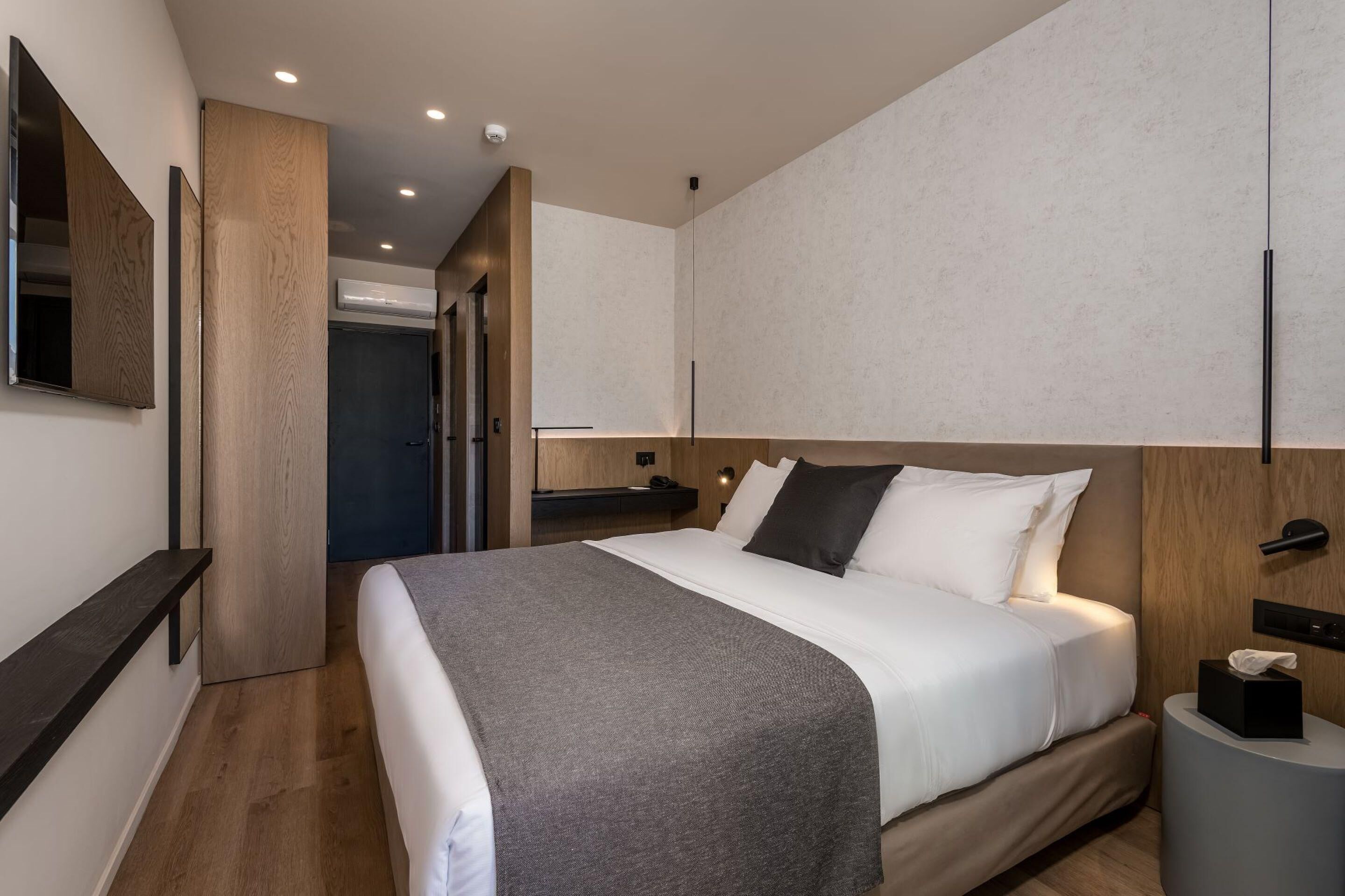 Une chambre d’hôtel moderne dotée d’un grand lit, d’une table de chevet, d’un téléviseur fixé au mur et d’une armoire intégrée.