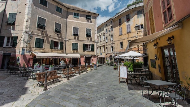 Una calle empedrada con mesas al aire libre y edificios con contraventanas.