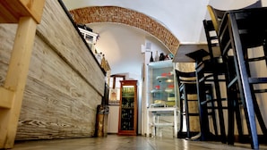 Un estrecho pasillo con una pared de madera en un lado y una vitrina de vidrio con botellas en el otro. Se ve una escalera con sillas negras al fondo.