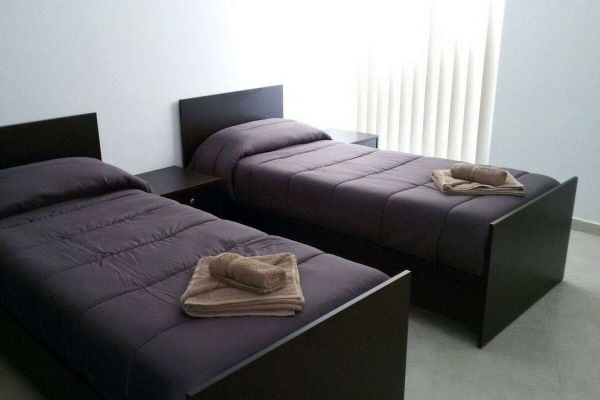Quarto de hotel moderno com duas camas de solteiro e uma pequena mesa.