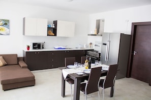 A modern kitchen with dark cabinets, a dining table set for four, and a brown sofa in the living area.