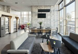 A modern lobby with a seating area, a mounted TV, and large windows offering a view of the street. - B&B HOTEL Paris Sud Châtenay Malabry (Chatenay-Malabry)