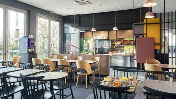 Un café moderne avec des tables et des chaises, un comptoir où sont exposés des produits alimentaires et un distributeur automatique.
