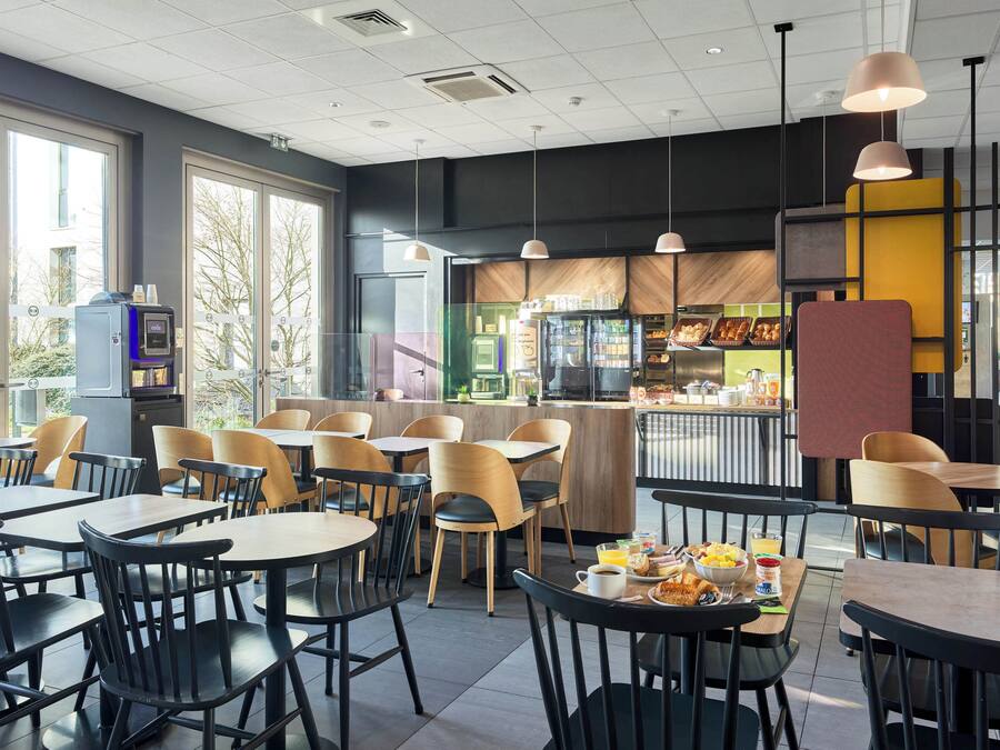 Un café moderne avec des tables et des chaises, un comptoir où sont exposés des produits alimentaires et un distributeur automatique.
