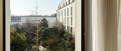 Vista desde una ventana que da a un patio con un edificio, un árbol y un sendero de piedra.
