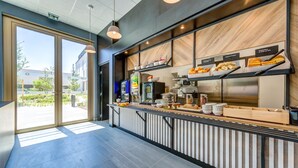 Una barra de desayuno moderna con una variedad de pasteles y bebidas, un amplio ventanal con vistas al exterior y un diseño limpio y contemporáneo.