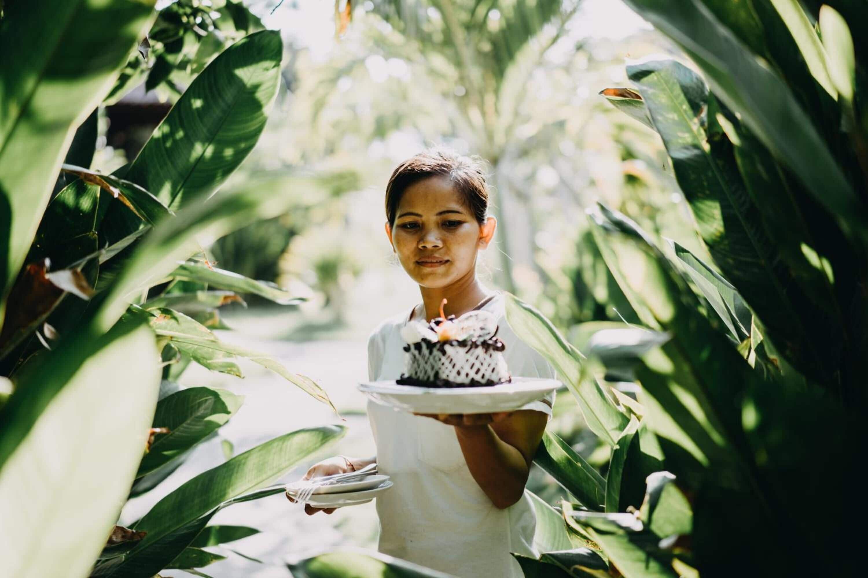 A person holding a plate with a cake in a lush, green environment.
