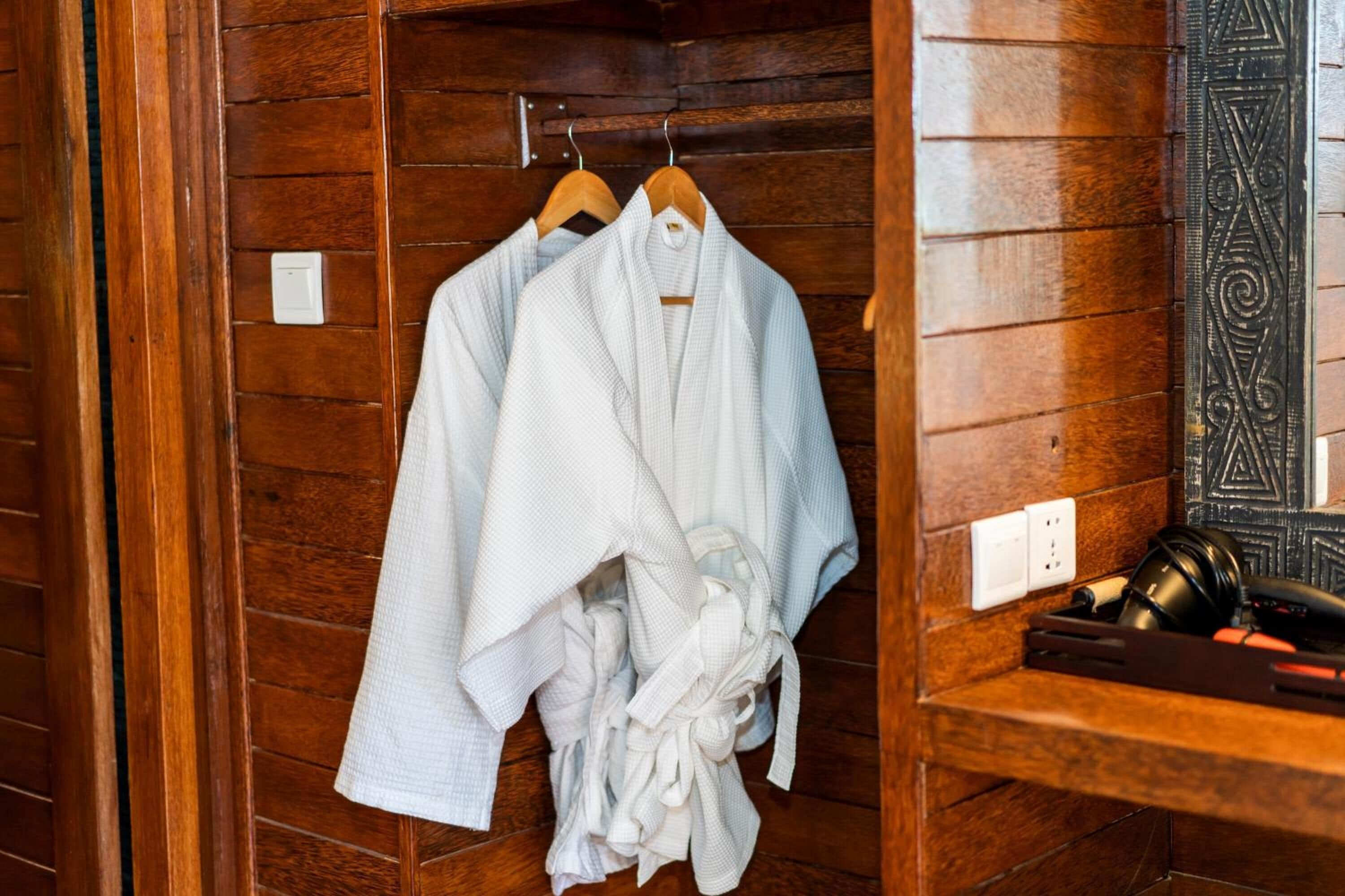 A wooden room with a robe rack holding several white robes.