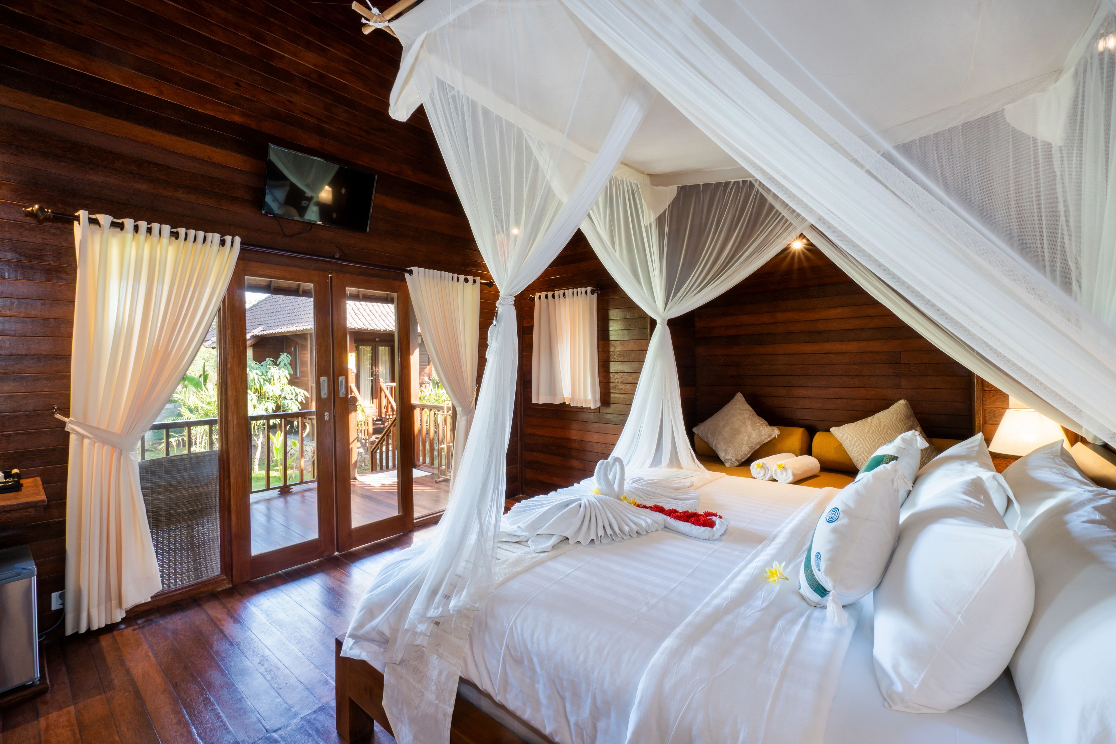 A room with a bed, white curtains, a wooden ceiling, and a balcony with glass doors.