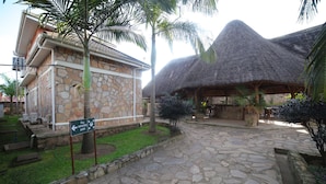 A stone building with a thatched roof, a fire assembly point sign, and a stone pathway. - Entebbe Palm Hotel (Entebbe)
