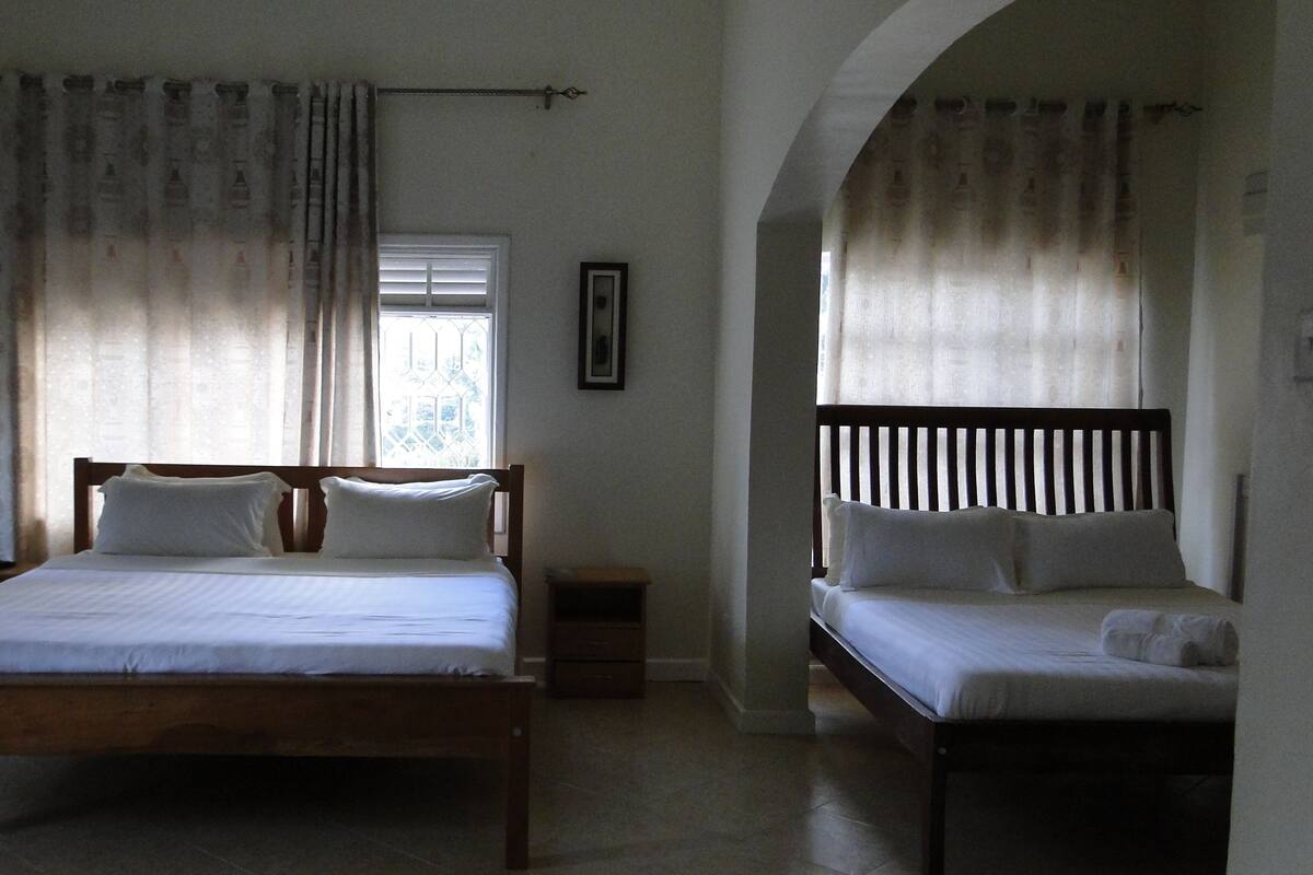 A bedroom with two beds, a window with curtains, a framed picture on the wall, and a wooden headboard.